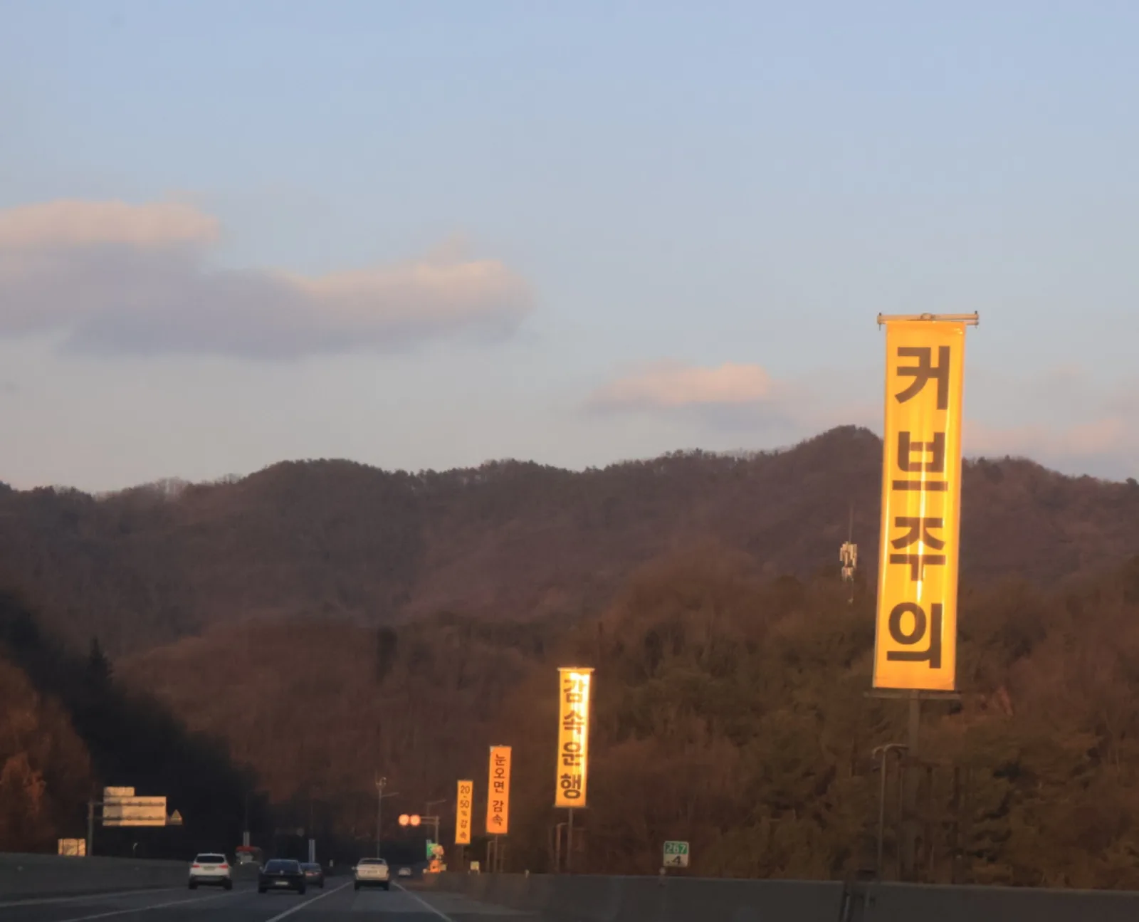 고속도로변에 '커브주의', '감속운행', '눈오면 감속'이라고 적힌 노란색 세로 현수막형 경고 표지판들이 잇따라 설치돼 있고, 도로 위로 승용차 여러 대가 주행하는 모습