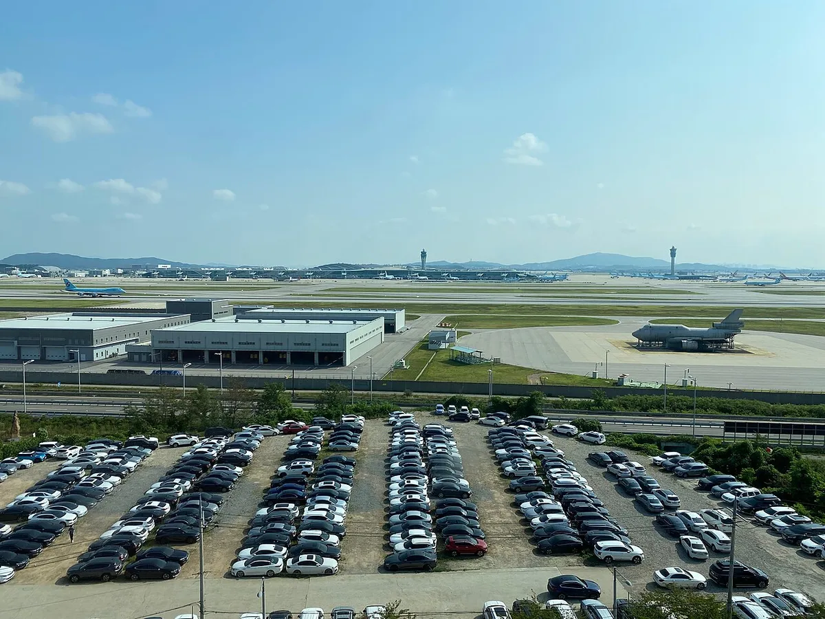 공항 인근의 넓은 노천 주차장에 승용차들이 빽빽하게 세워져 있고 멀리 공항 관제탑이 보이는 모습