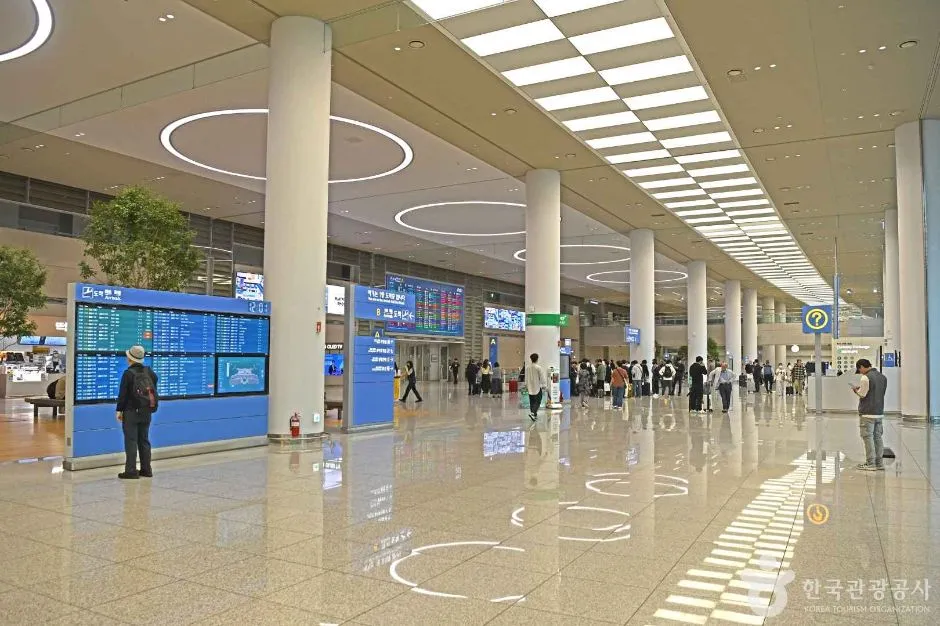 공항 터미널 내부의 밝은 출국 로비와 안내 전광판 앞에 서 있는 이용객들