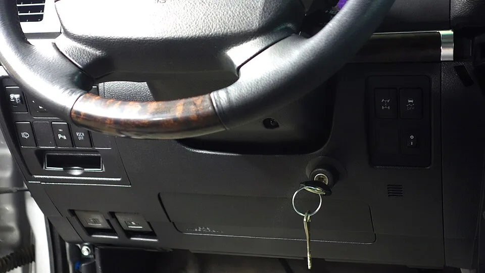 SUV 차량 실내에서 스티어링 휠 아래 이그니션 키 배럴에 열쇠가 꽂혀 있고 열쇠고리가 매달려 있는 클로즈업