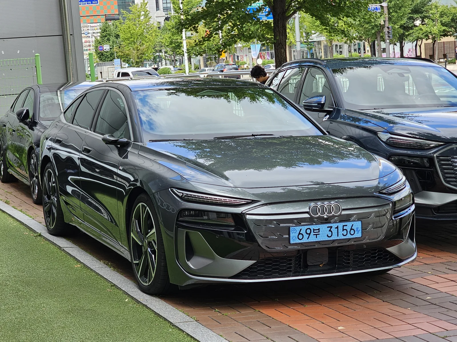 주차된 짙은 회색 아우디 A6 스포트백 e-트론의 전면 클로즈업, 싱글프레임 그릴에 새겨진 아우디 링 엠블럼이 보인다