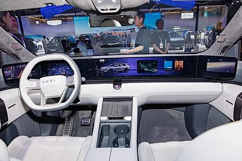 아우디 E7X 실내, 넓은 파노라믹 디스플레이와 스티어링 휠에 새겨진 AUDI 레터링 로고가 보인다