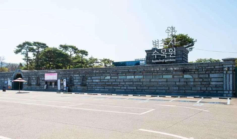 회색 석축 담장 위에 벽초지수목원 간판이 올라가 있고 앞쪽에 넓은 포장 공간이 있는 입구