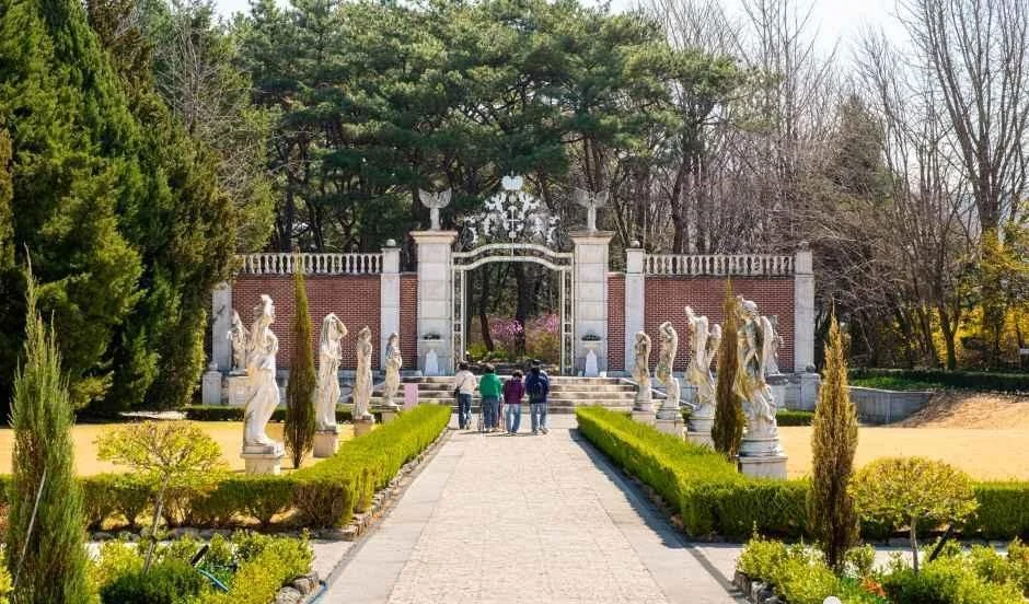 벽돌 담과 철제 문 앞으로 흰 조각상이 늘어선 벽초지수목원의 유럽식 정원 산책로