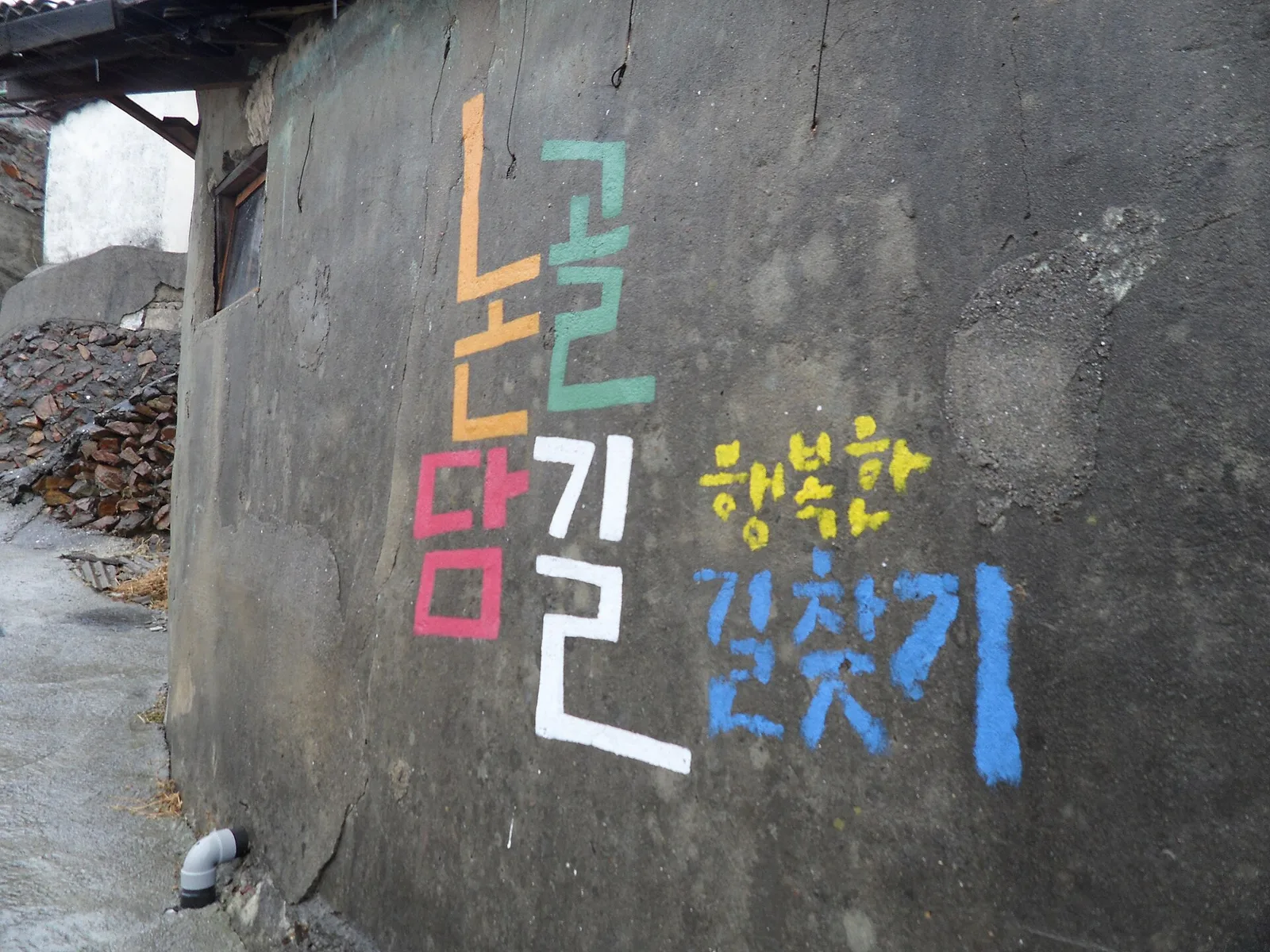 회색 시멘트 담벼락에 알록달록한 색으로 논골담길 행복한 길찾기라는 글씨가 쓰여 있다