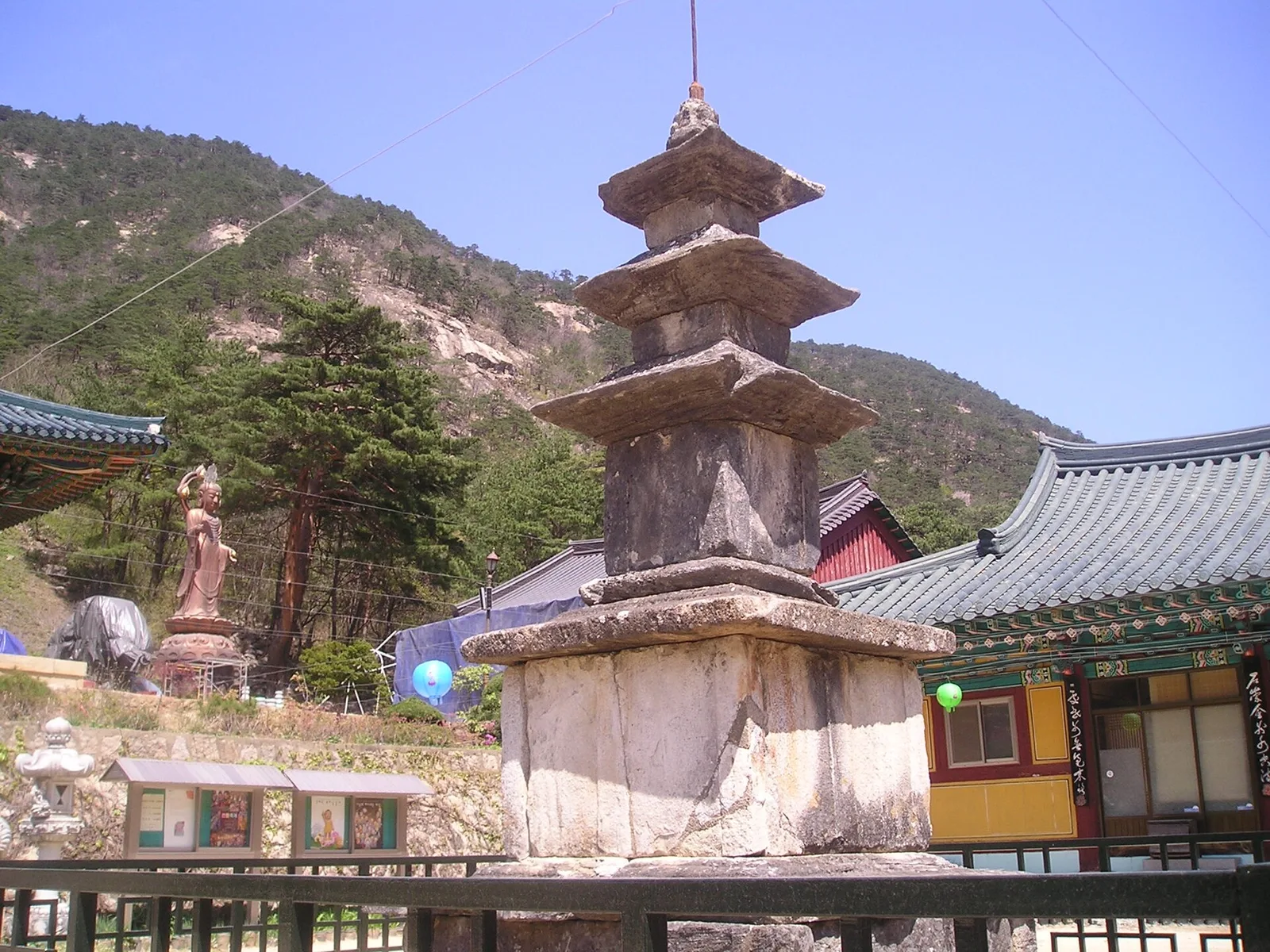 사찰 마당에 선 오래된 삼층석탑 뒤로 기와 건물과 바위산이 보인다