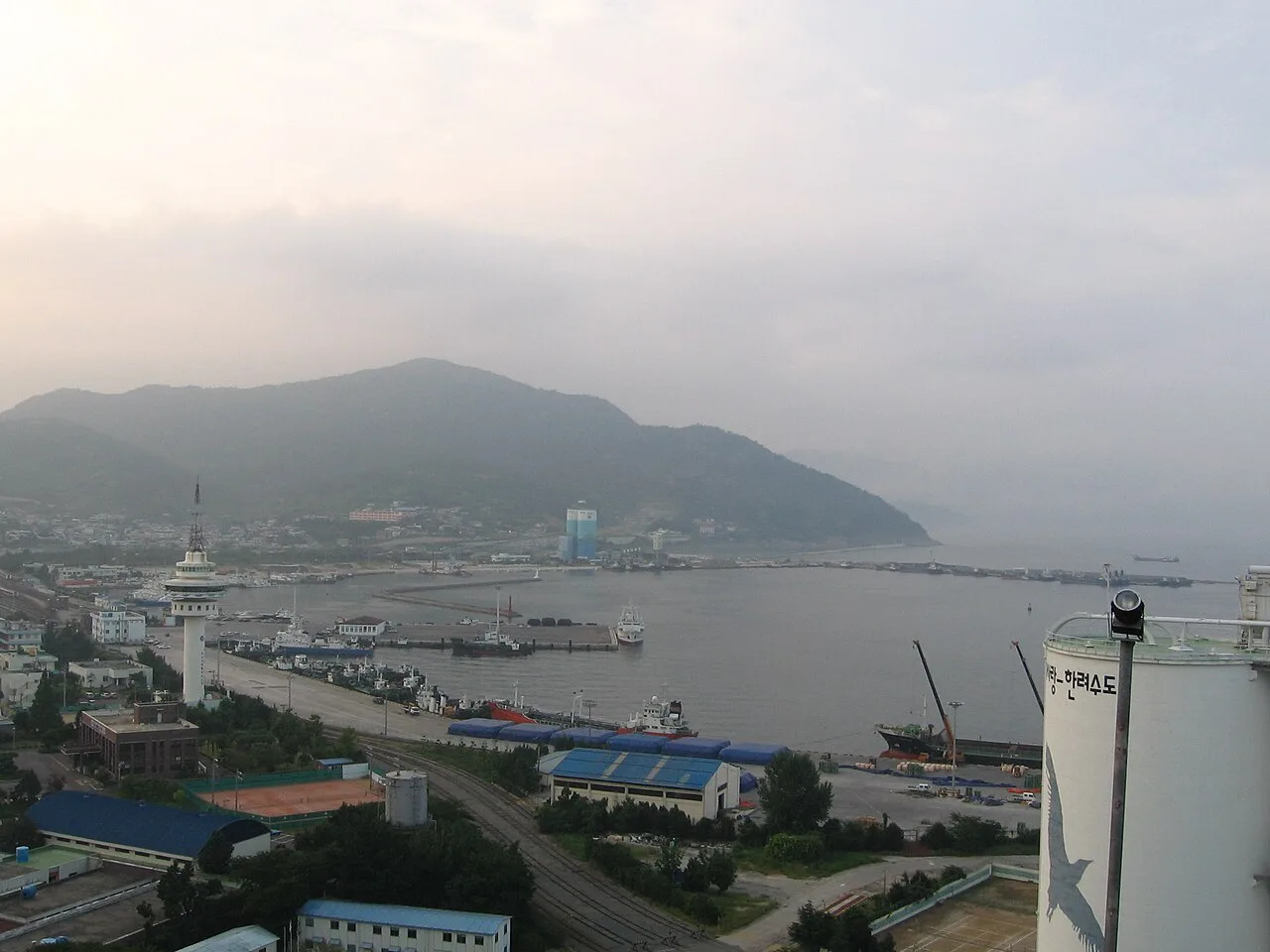 여수항 부두에 정박한 배들과 주변 건물, 산으로 둘러싸인 항구 전경