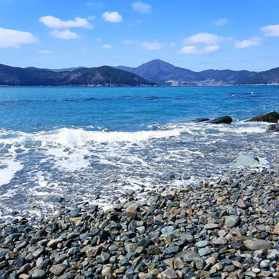 푸른 바다 너머로 먼 산줄기가 보이는 지심도 몽돌 해변