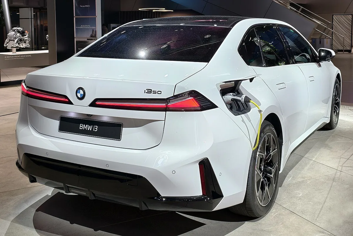 전시장에 세워진 흰색 BMW i3 50의 뒷모습, 충전 케이블이 꽂혀 있고 트렁크 리드에 i3 50 로고가 있다