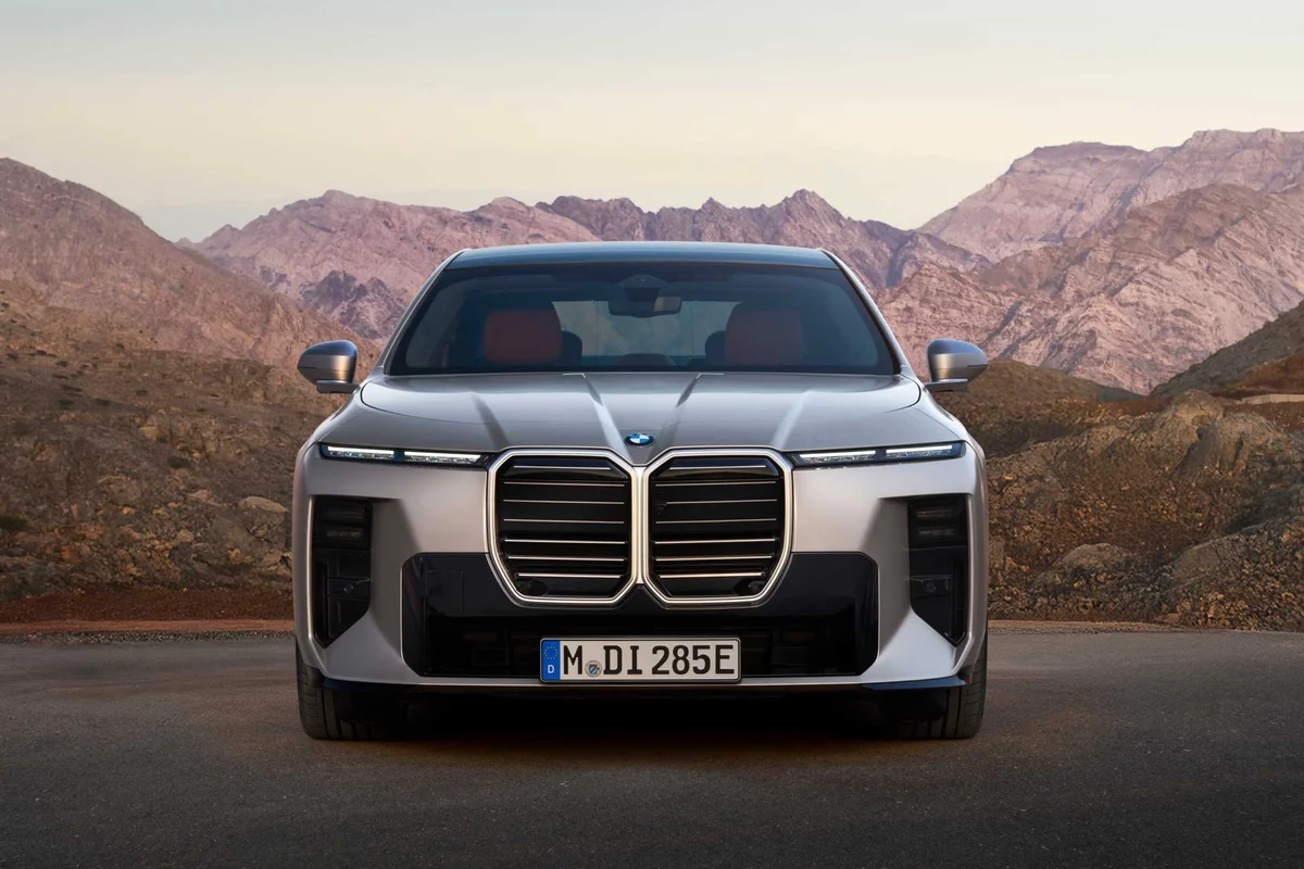 산악 도로 앞에 선 BMW i7 60 xDrive 전면, 슬림한 헤드램프와 큰 키드니 그릴