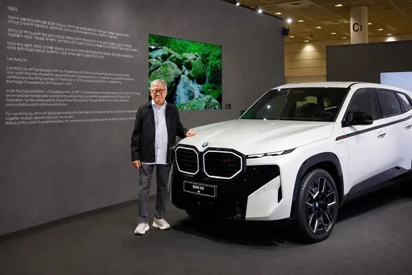 이강소 작가가 BMW XM 레이블 옆에 서 있는 모습, 뒤로 작가 소개 텍스트와 풍경화가 걸려 있다