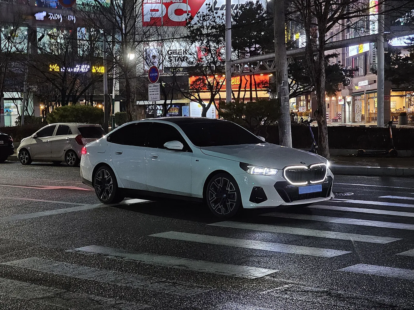 밤거리 횡단보도 앞에 선 흰색 BMW i5 전면, 점등된 키드니 그릴 테두리가 보인다