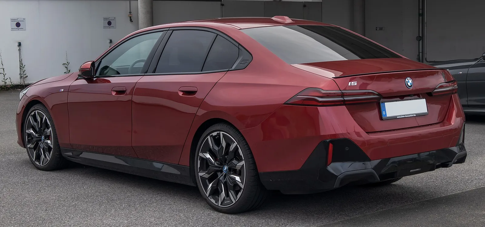 붉은색 BMW i5(G60) xDrive40 M 스포츠 프로 후면 3/4, 낮은 테일램프와 대형 휠이 보인다