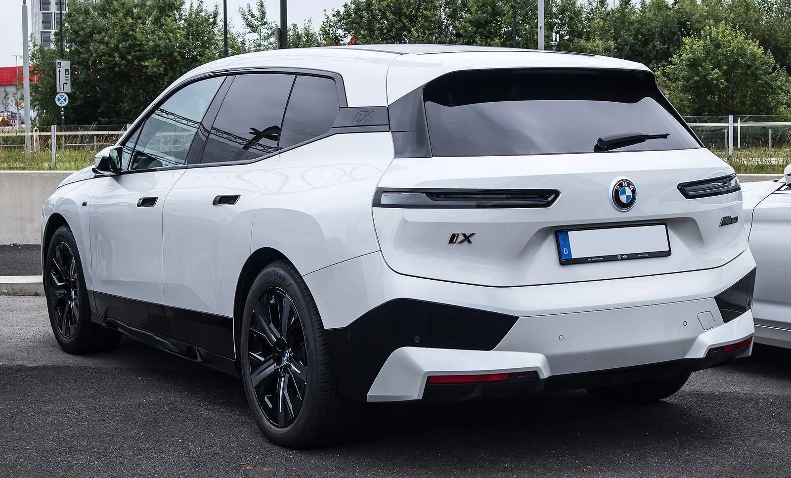 흰색 BMW iX 후면 3/4, 낮게 이어진 테일램프와 iX 레터링이 보인다