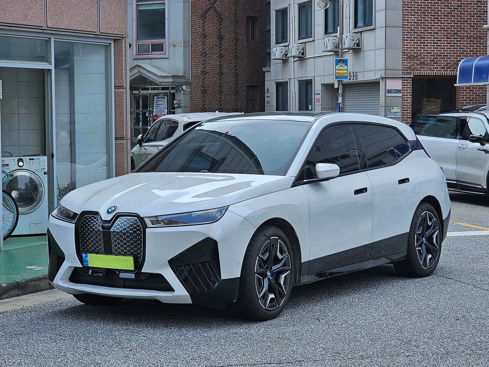 도심 골목에 주차된 흰색 BMW iX 전면, 대형 키드니 그릴이 보인다
