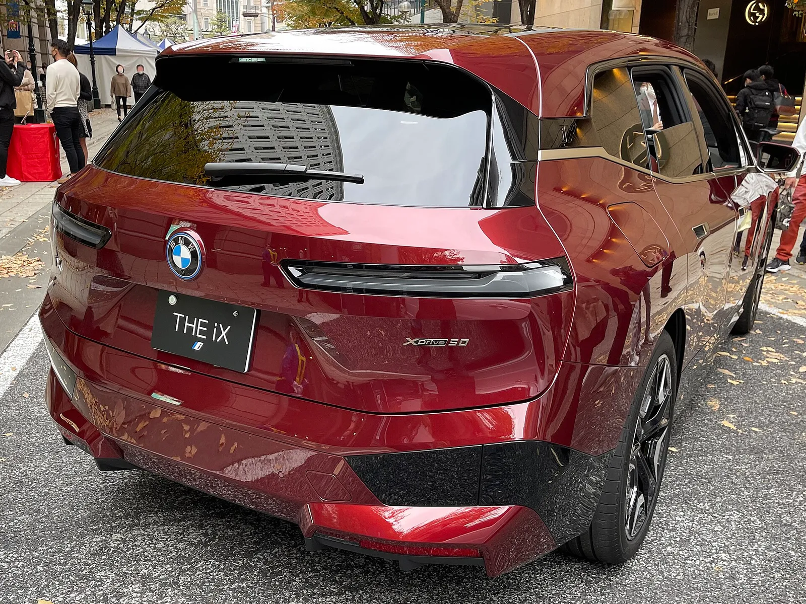 붉은색 BMW iX xDrive50 후면, 일체형 테일게이트와 가는 테일램프, 낮은 범퍼가 보인다