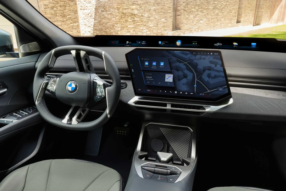 BMW iX4 50 xDrive 실내, 스티어링 휠과 대형 센터 디스플레이, 앞유리 하단의 파노라믹 비전이 보인다