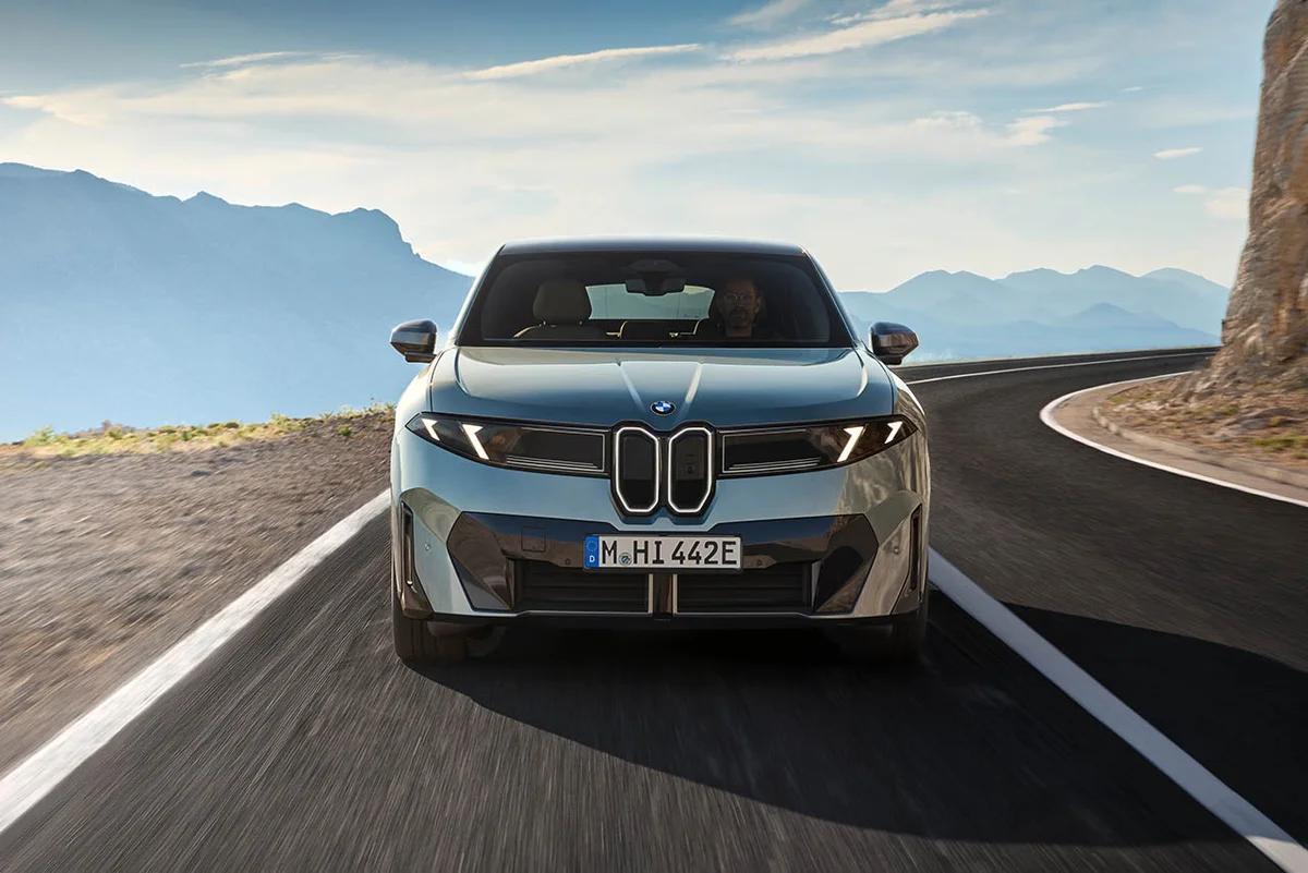 회색 BMW iX4 50 xDrive 정면, 산악 해안 도로를 달리는 모습
