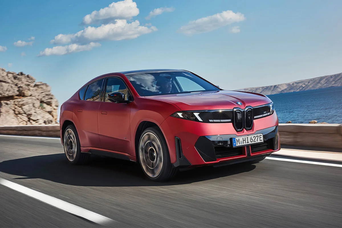 빨간색 BMW iX4 M60 xDrive가 바닷가 도로를 달리는 전면 3/4 모습