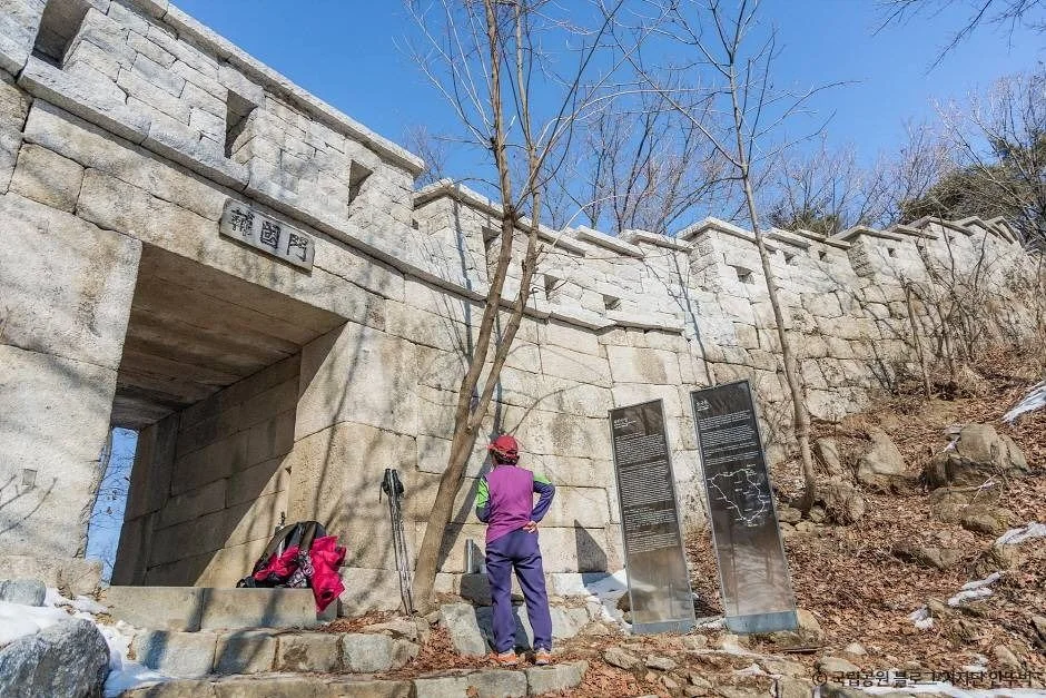 성문과 성벽 앞에 선 탐방객, 마른 가지와 낙엽이 쌓인 북한산성