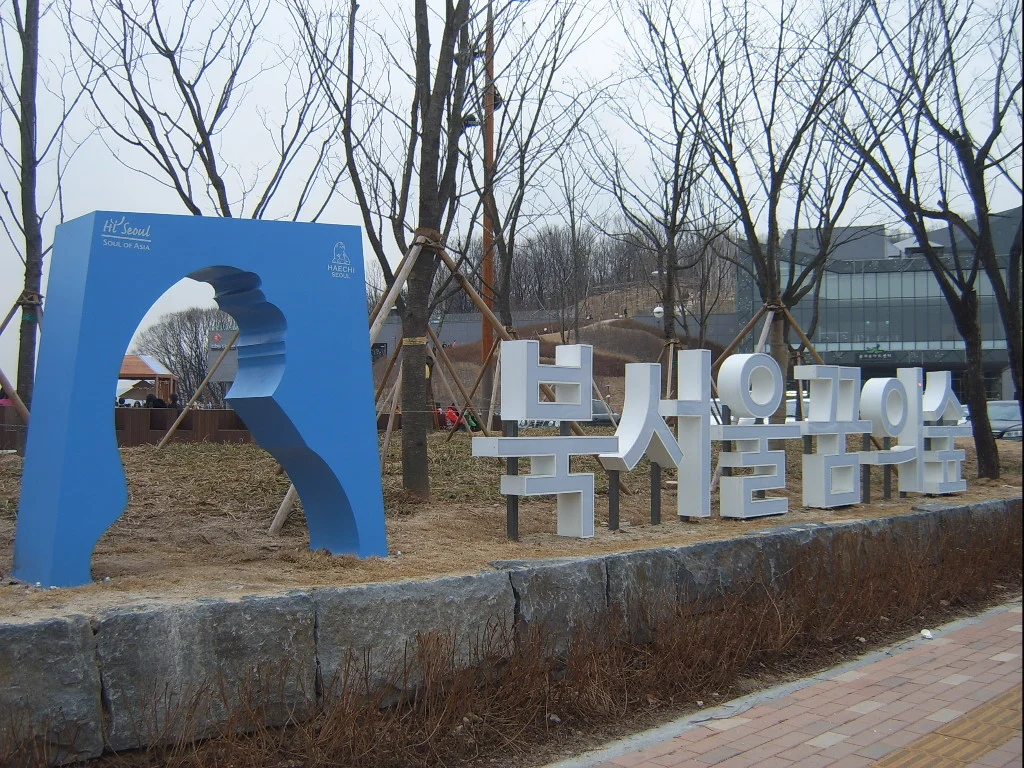 잎이 진 나무 사이에 서 있는 북서울꿈의숲 표지 조형물