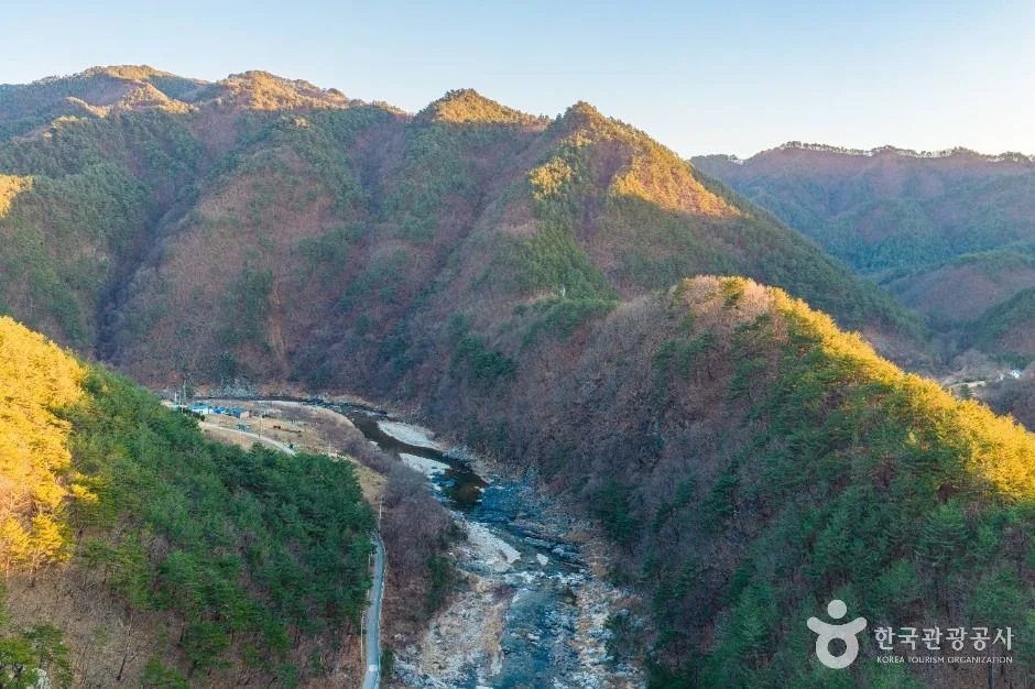 능선과 골짜기가 겹겹이 이어지고 아래에 하천이 흐르는 산악 지형 항공 사진