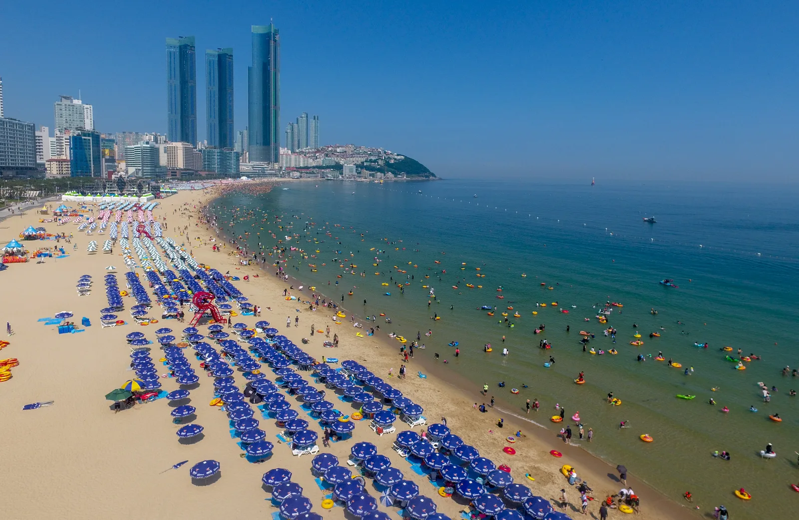 파라솔이 빼곡히 늘어선 부산 해운대 해변 항공 전경과 해변가 고층빌딩