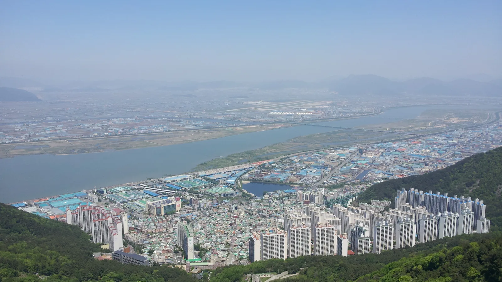 부산 사상구 엄궁동 일대에서 내려다본 낙동강과 주변 시가지, 강 건너편으로 공단과 아파트 단지, 김해공항 활주로가 보인다