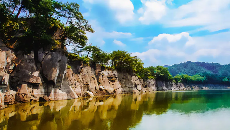 세로로 갈라진 회색 암벽 위에 소나무가 자라고, 잔잔한 호수 수면에 암벽이 그대로 비친 모습