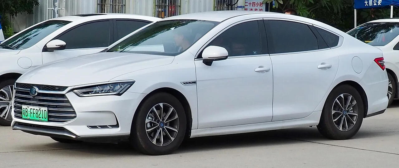 흰색 BYD 친 세단의 전면 및 측면 모습, 반사형 헤드램프와 크롬 그릴이 보인다