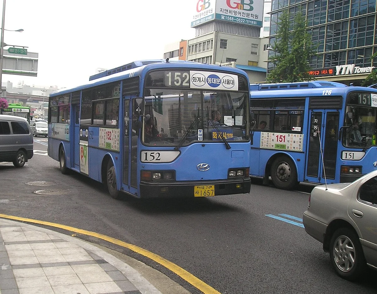 파란색 서울 시내버스 152번이 정류장 앞 도로에서 정차해 있고 뒤에 151번 버스가 보이는 모습