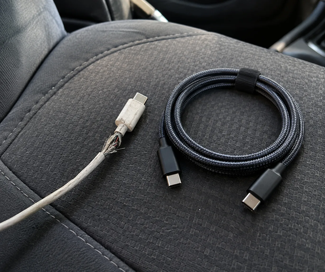 차 시트 위에 커넥터 근처 피복이 벗겨진 흰색 케이블과 새 검은색 브레이드 USB-C 케이블이 나란히 놓여 있다(AI 생성 이미지)