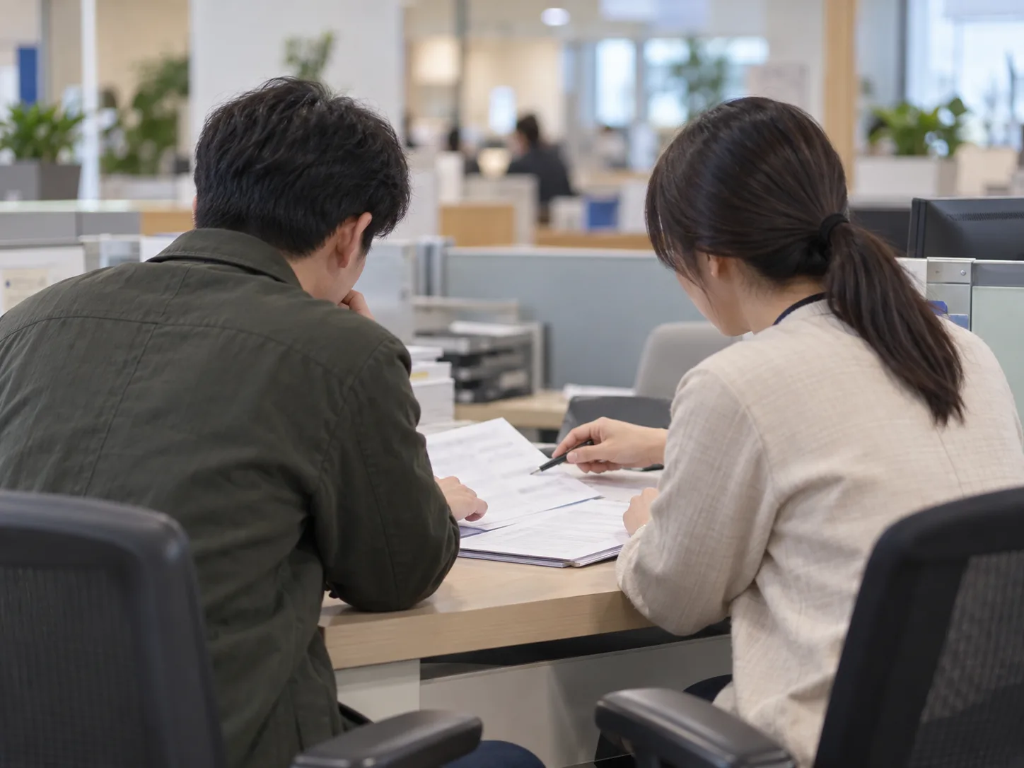 상담 창구에서 상담원과 고객이 서류를 함께 보며 상담하는 뒷모습 장면