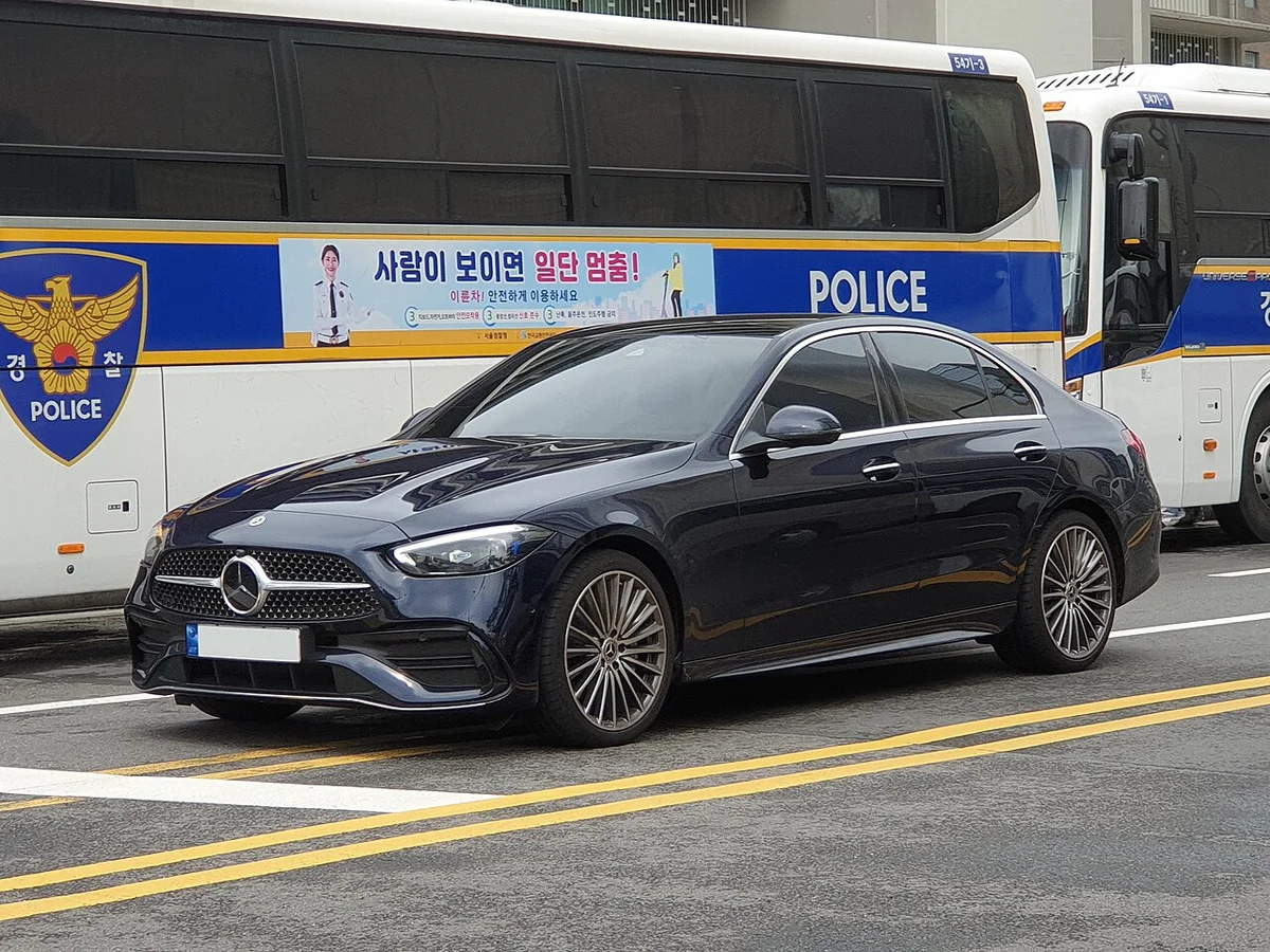 경찰 버스 옆 도로에 선 짙은 파란색 벤츠 C 300 AMG 라인(W206)의 전면 3/4