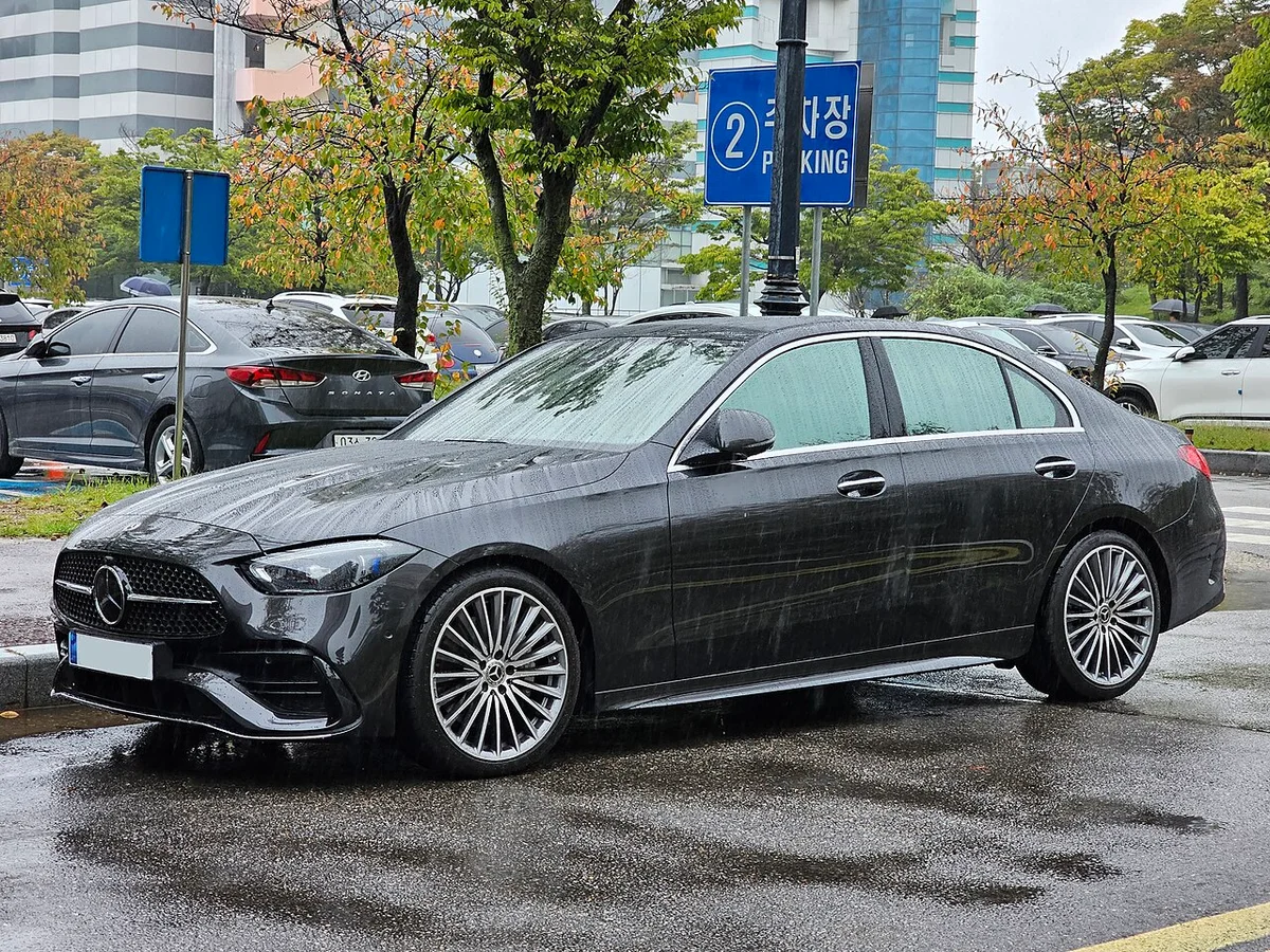 비 오는 날 주차장에 선 짙은 회색 벤츠 C 300 4MATIC AMG 라인(W206)의 전면 3/4