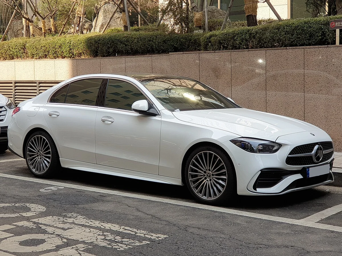 주차 구역에 선 흰색 벤츠 C 300 4MATIC AMG 라인(W206)의 전면 3/4, 다이아몬드 패턴 그릴
