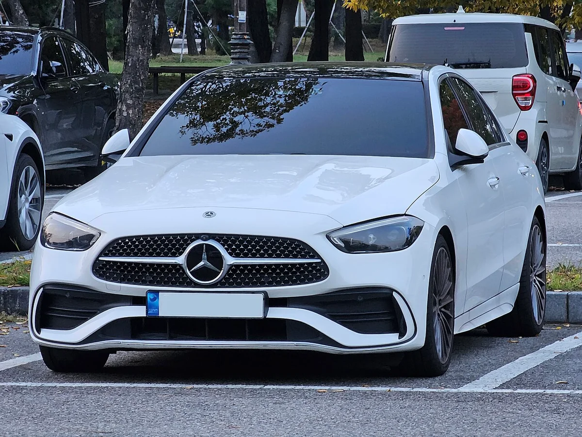주차선 안에 정면으로 선 흰색 벤츠 C-Class(W206) AMG 라인, 다이아몬드 패턴 그릴과 전면 범퍼