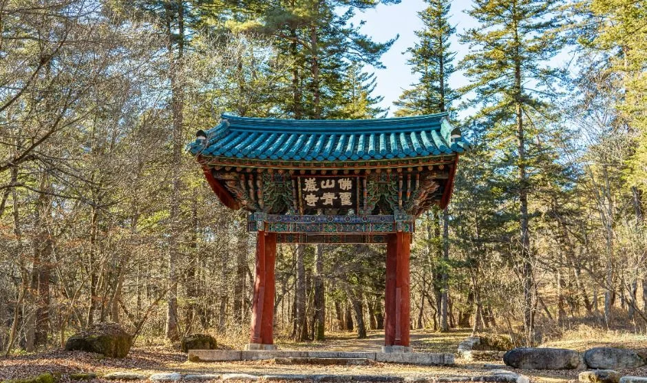 숲을 배경으로 청록색 지붕을 얹은 붉은 기둥의 문 형태 건물