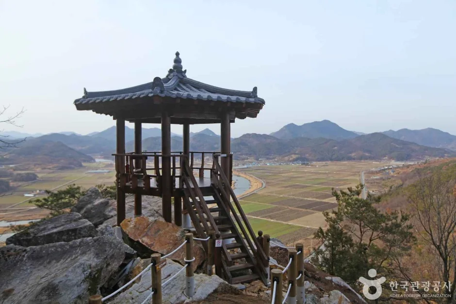 바위 위에 세워진 한옥 정자와 멀리 보이는 들판