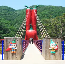 청양 천장호출렁다리 입구의 붉은 고추 모양 주탑과 다리 양옆에 세워진 마스코트 인형