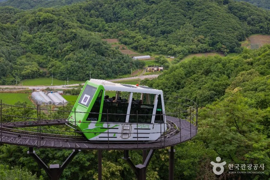 푸른 산자락 아래 원형 승강장에 서 있는 연두색 모노레일 차량
