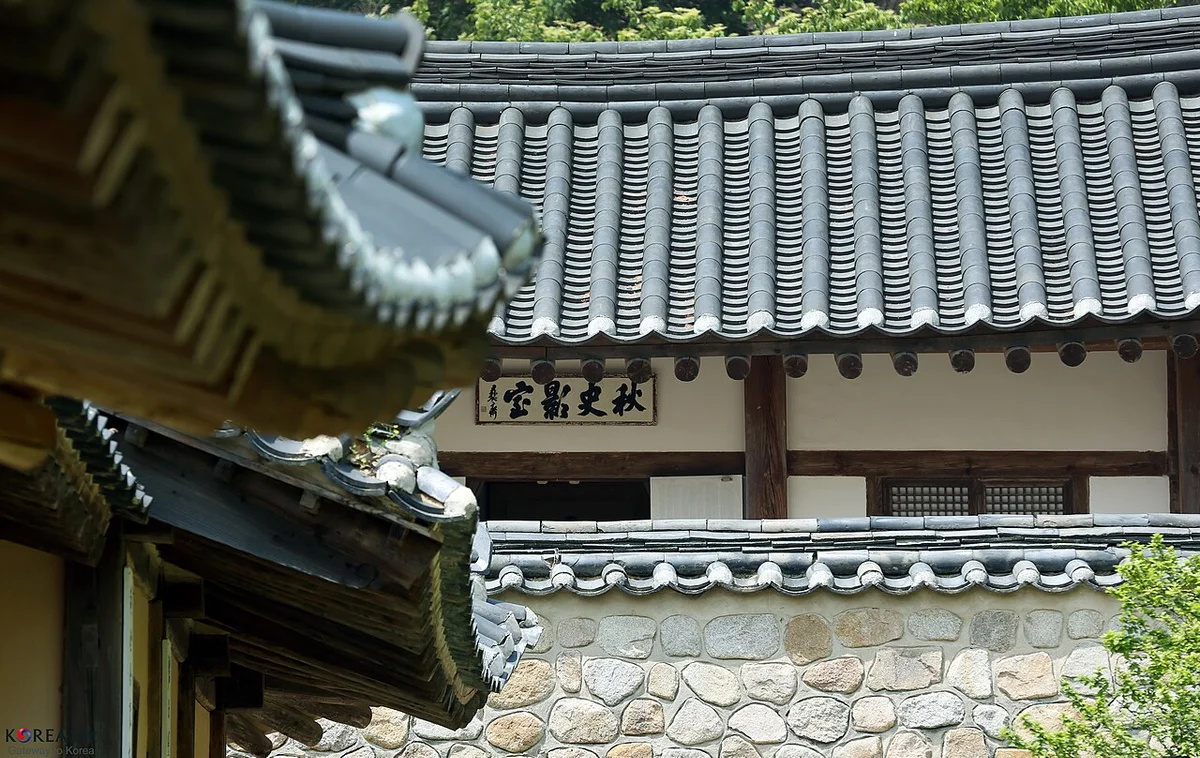 편액이 걸린 건물과 돌담 위로 처마가 보이는 추사고택