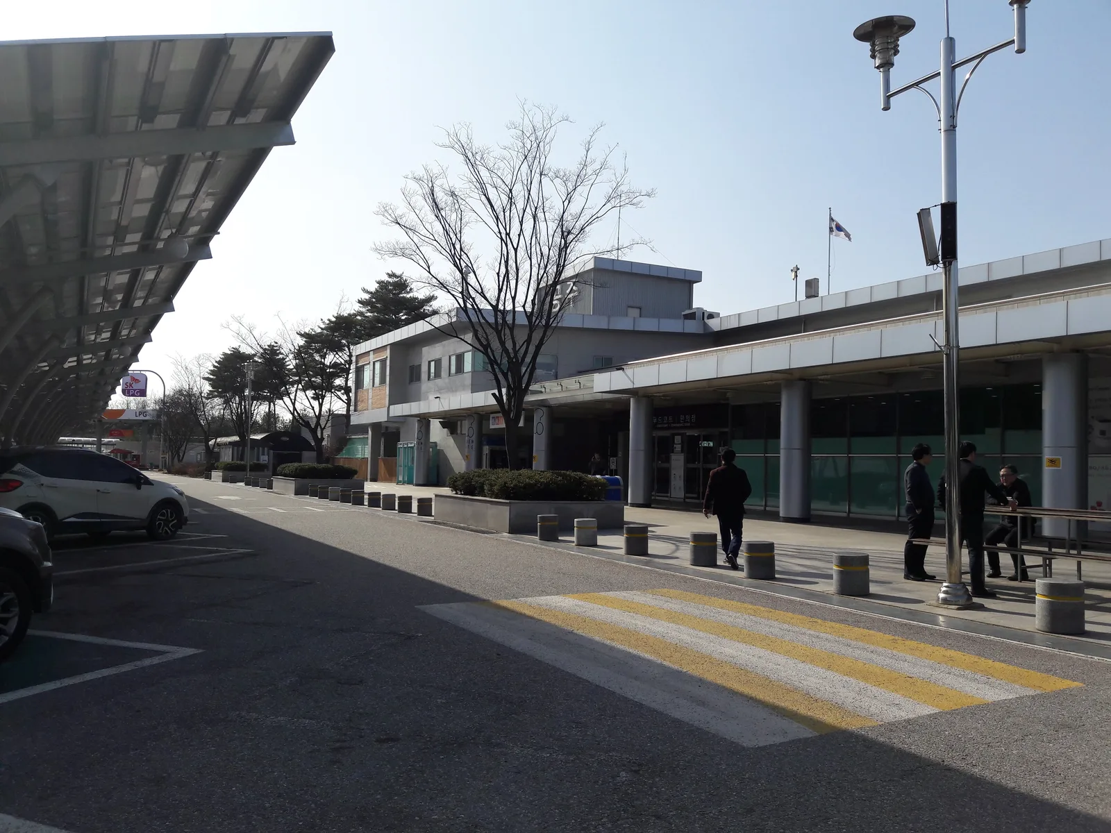 고속도로 휴게소 건물 앞 광장에서 사람들이 걸어다니고 주유소 캐노피가 보이는 모습