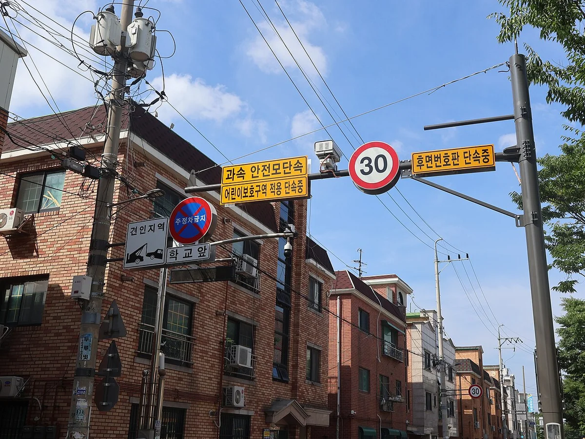 도로 위 전봇대 지지대에 시속 30 제한 표지와 어린이보호구역 단속 안내 표지가 걸려 있는 모습