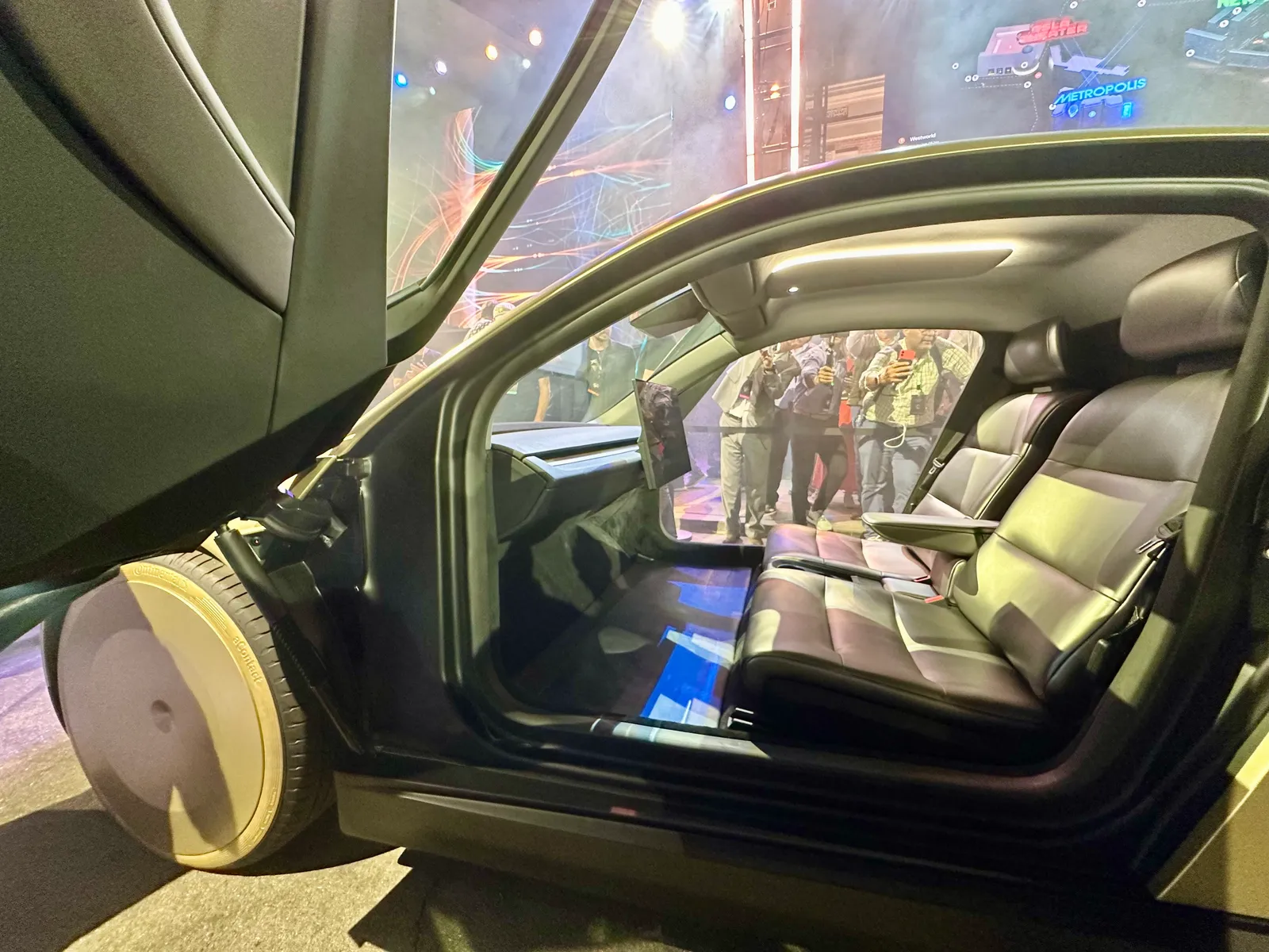 걸윙 도어가 열린 사이버캡 실내, 좌석과 좁은 뒷좌석 공간, 대시보드 일부가 보이며 창밖으로 취재진의 모습이 비친다