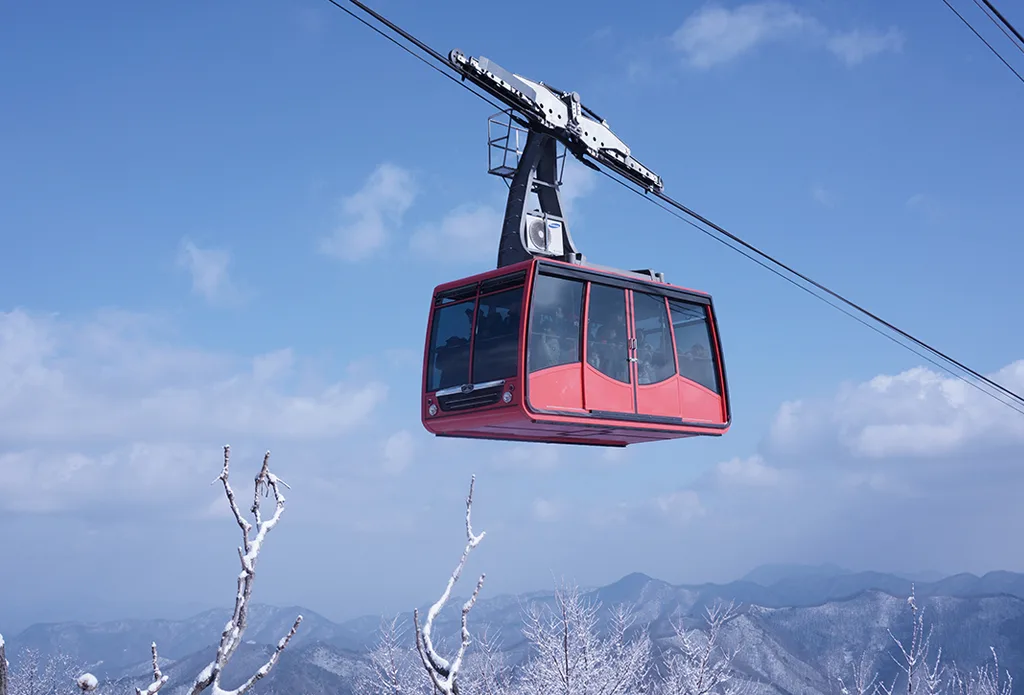 파란 하늘을 배경으로 케이블에 매달린 대둔산케이블카 빨간색 곤돌라가 산 능선을 지나는 모습