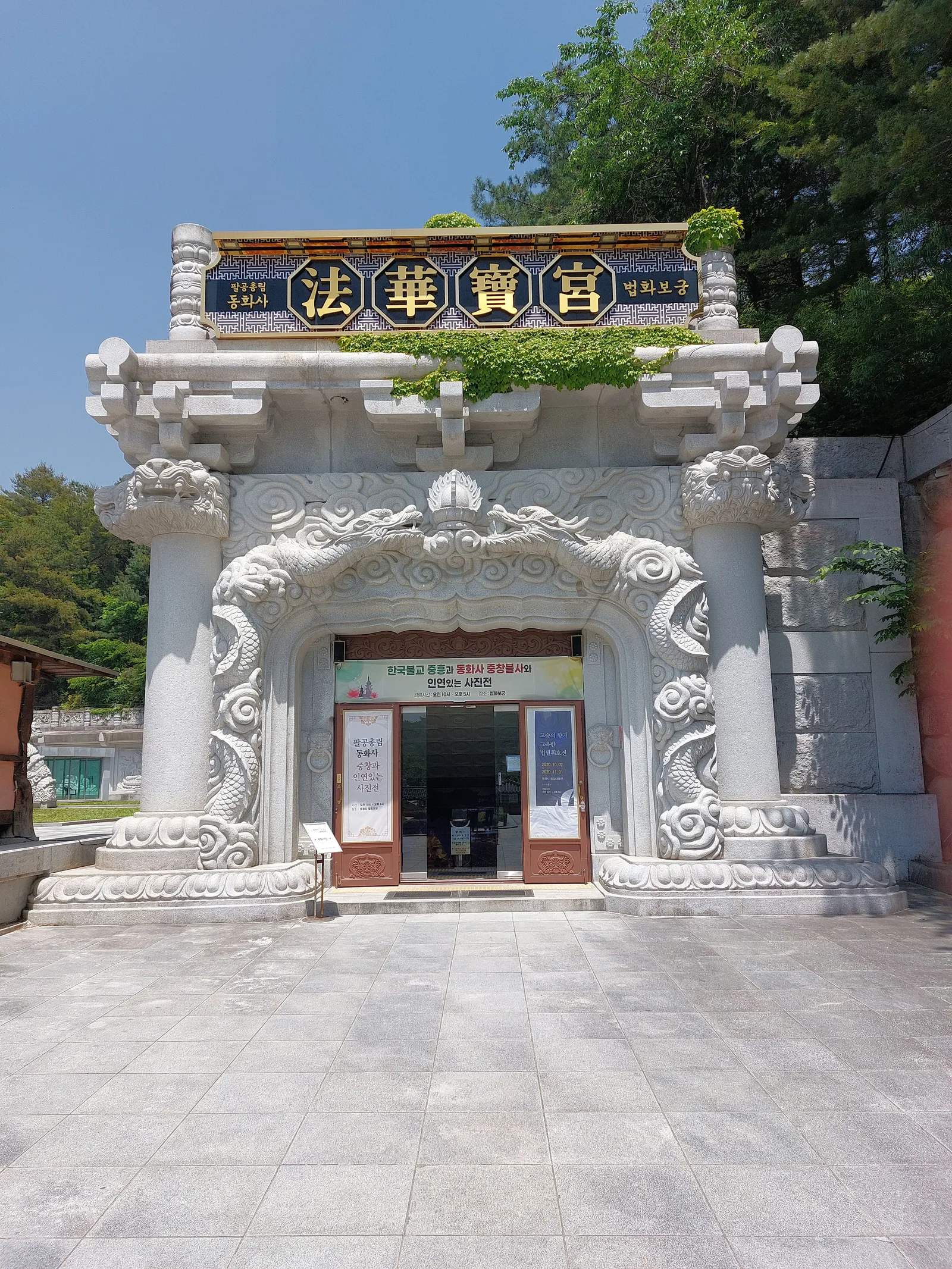 용 조각이 새겨진 화강암 돌기둥과 '법화보궁' 현판이 걸린 동화사 통일대불 경내 입구, 계단 위 석조 문 구조물