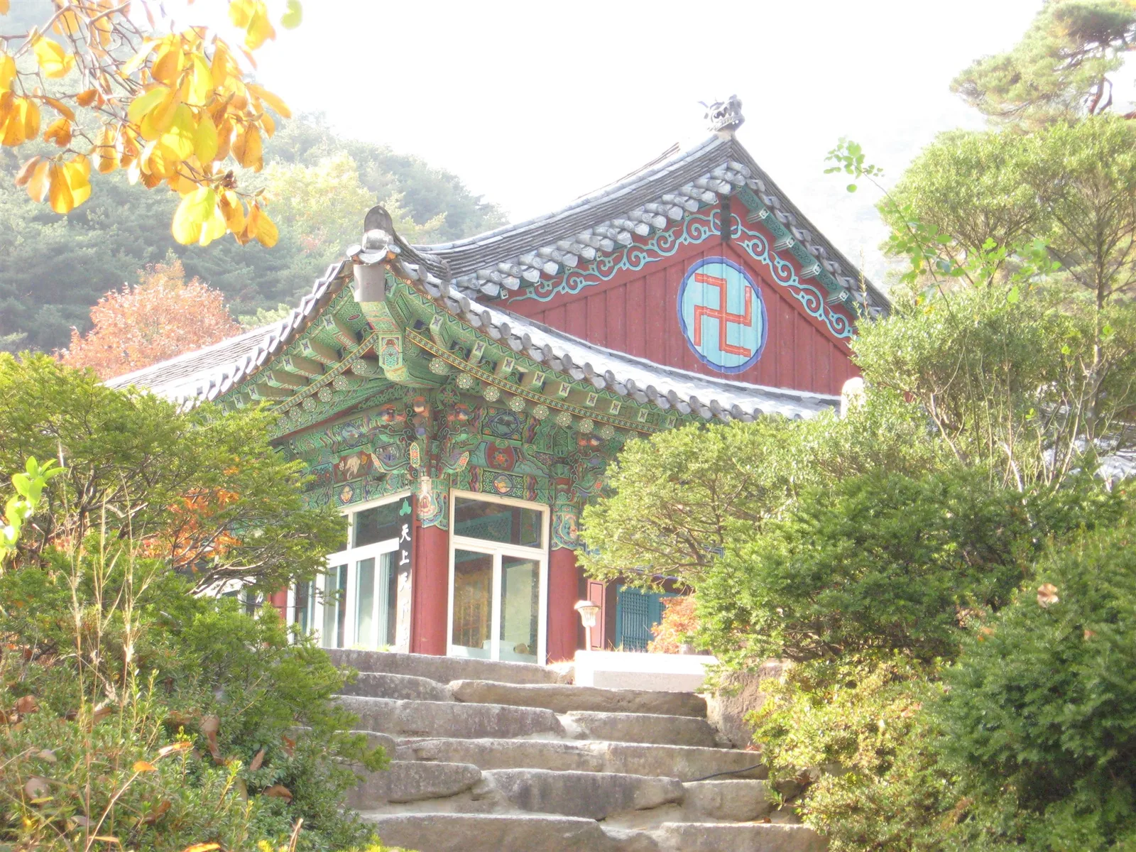 소나무와 단풍나무 사이로 보이는 팔공산 파계사 전각, 처마에 만(卍)자 문양이 새겨져 있고 앞에 돌계단이 있다