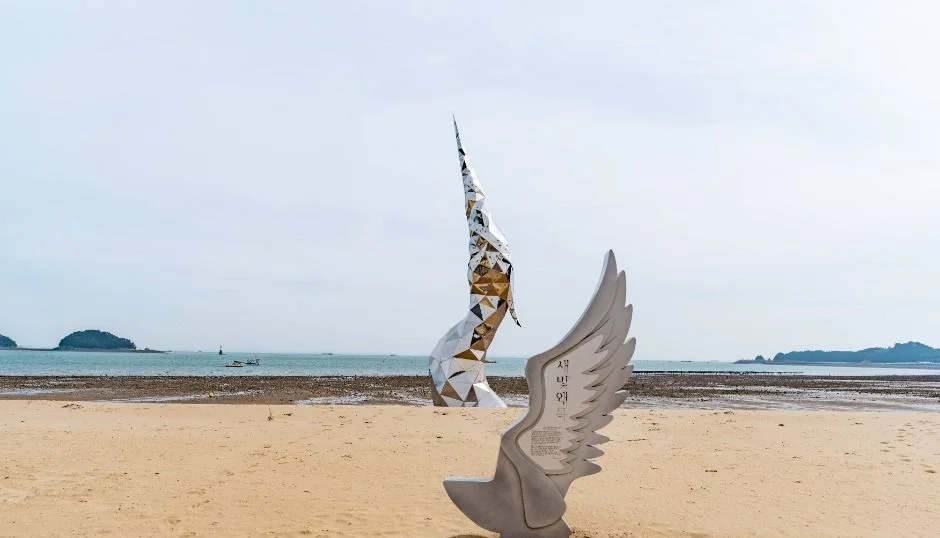 왜목마을 모래 해변에 서 있는 날개 모양 조형물과 먼 바다의 섬