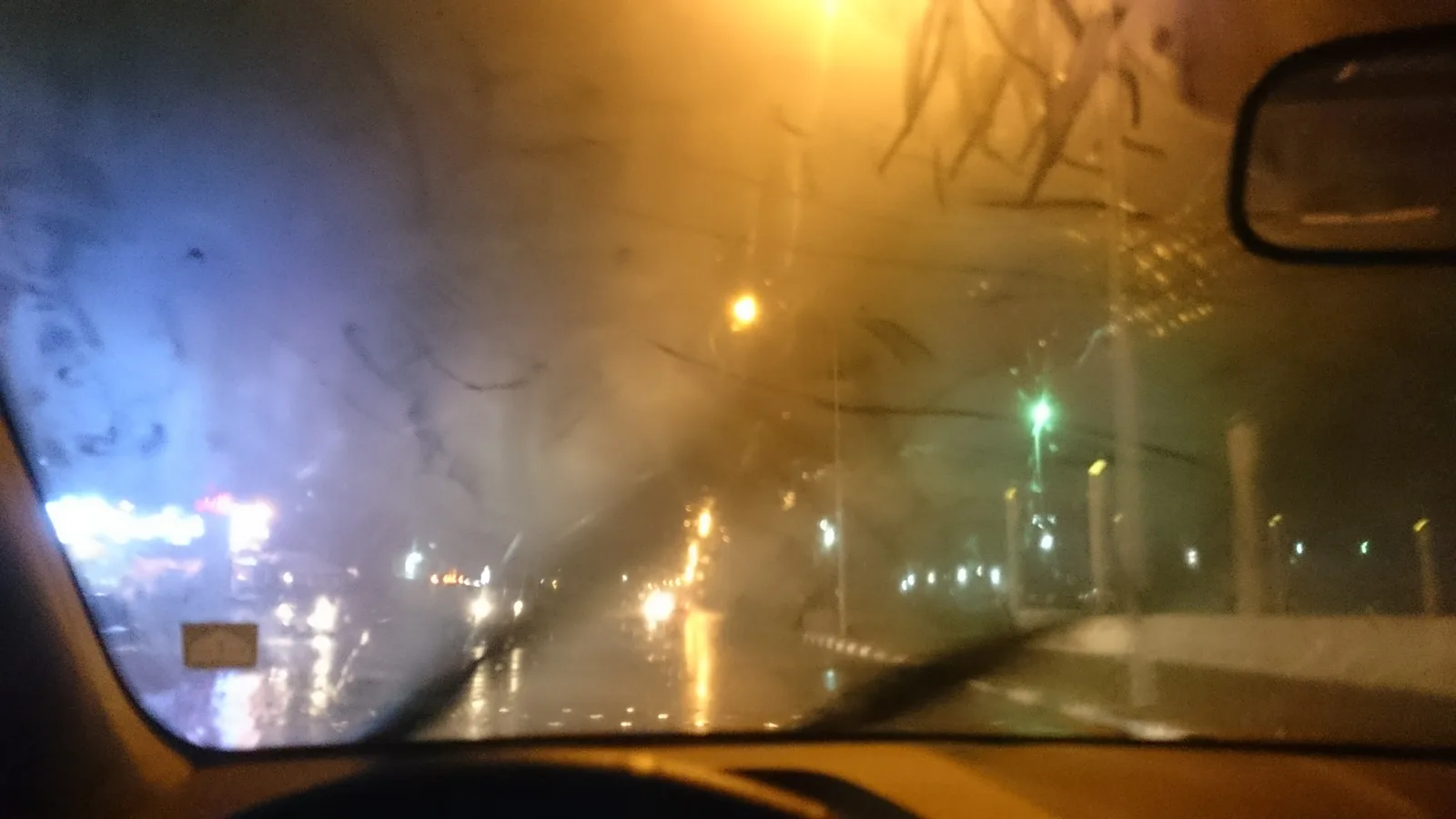 비 오는 밤 자동차 안에서 바라본 앞유리 전체가 김과 빗물로 뿌옇게 흐려져 도로와 신호등 불빛이 번져 보이는 모습